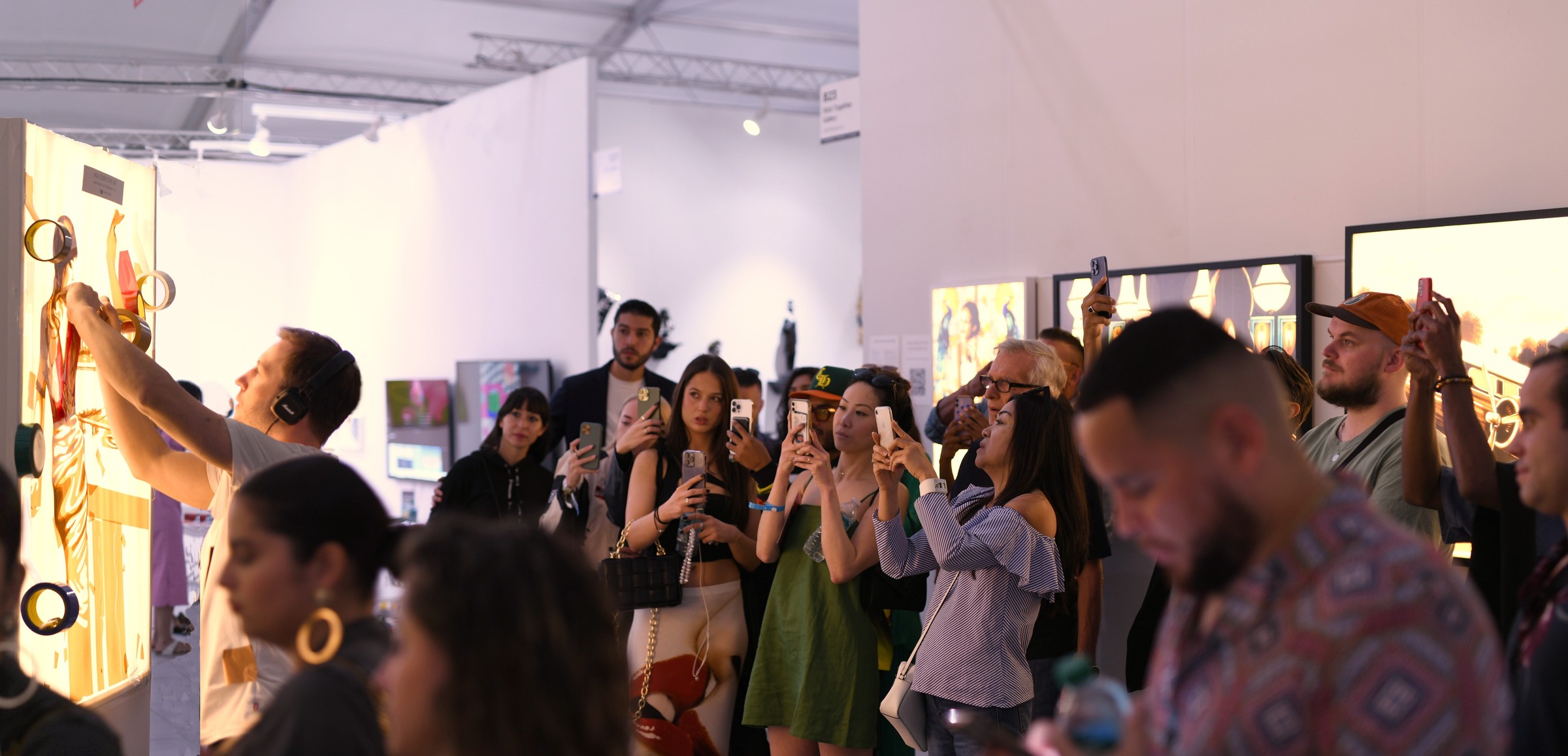 Visitors watch and photograph Max Zorn creating an illuminated tape artwork at an international art fair.
