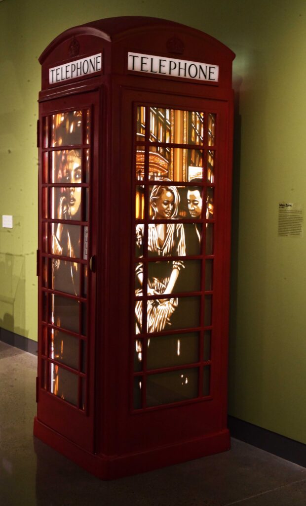 Museum exhibit featuring Max Zorn’s glowing tape artwork installed inside a classic red telephone booth, displayed in a gallery setting.